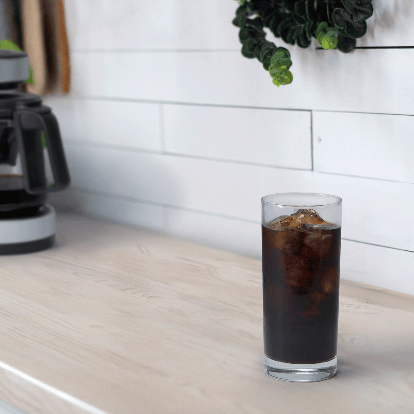 A tall cup of iced coffee is on a kitchen countertop, with the EC-DAC50 Coffee Maker in the background.