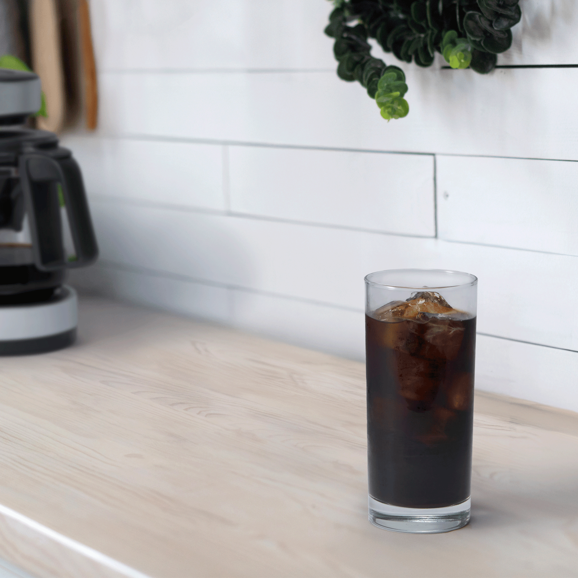 A tall cup of iced coffee is on a kitchen countertop, with the EC-DAC50 Coffee Maker in the background.
