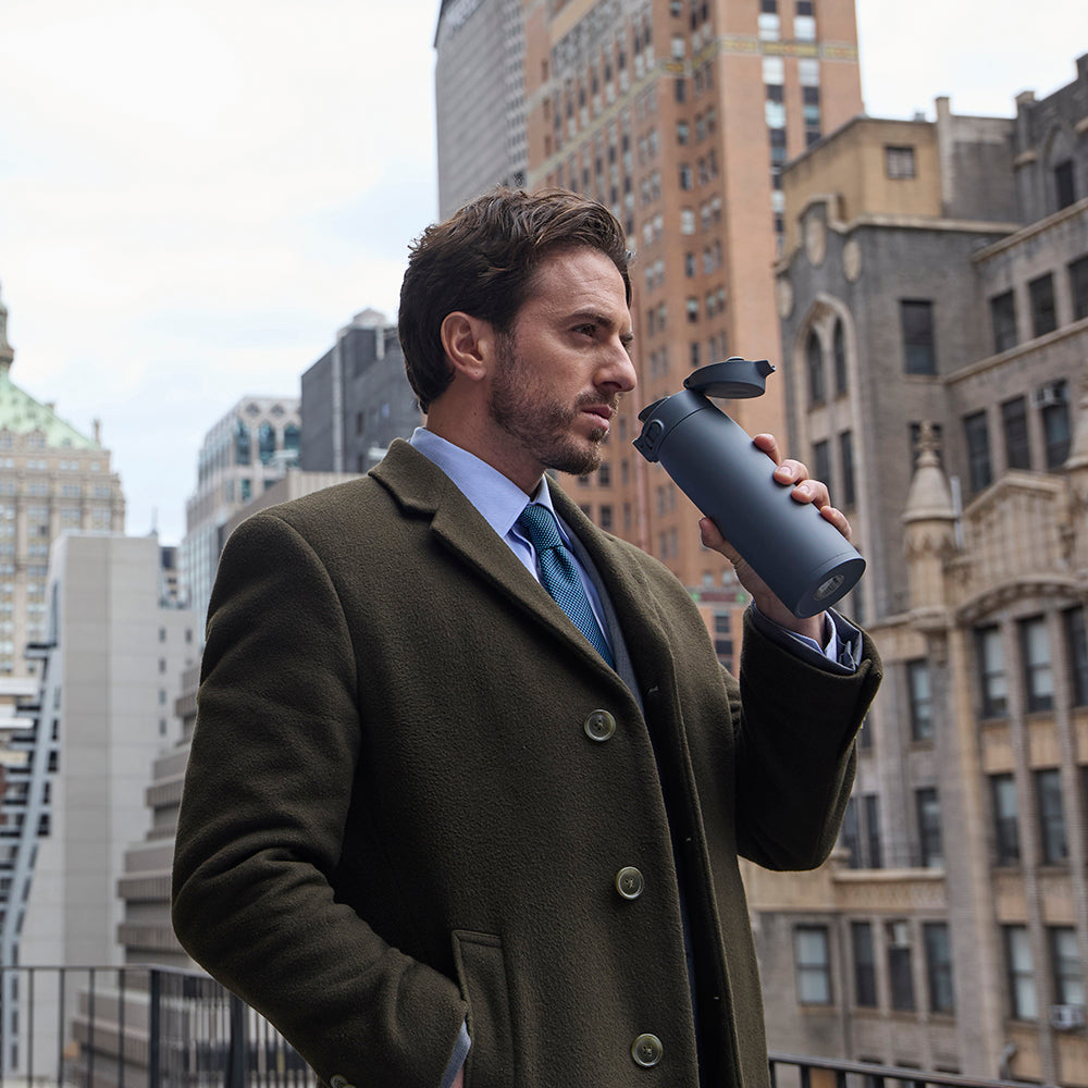 Man in a coat holding a GoCafe against a cityscape background