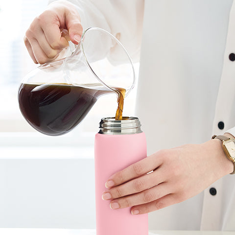 Person pouring coffee from a glass pitcher into a pink thermos.