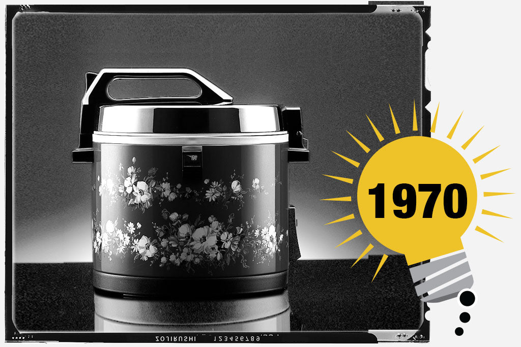 Black and white photo of the first Zojirushi  Rice Warmer. The unit has  floral print on its body.  Photo is labeled with the year, 1970. 