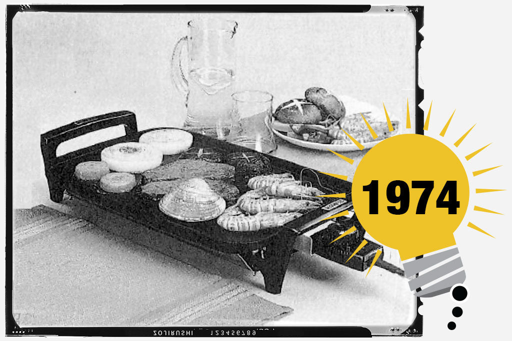 Black and white photo of Zojirushi’s first Electric Hot Plate. The unit has onion, onion. Shrimp, clams and other foods. Photo is labeled with the year 1974.