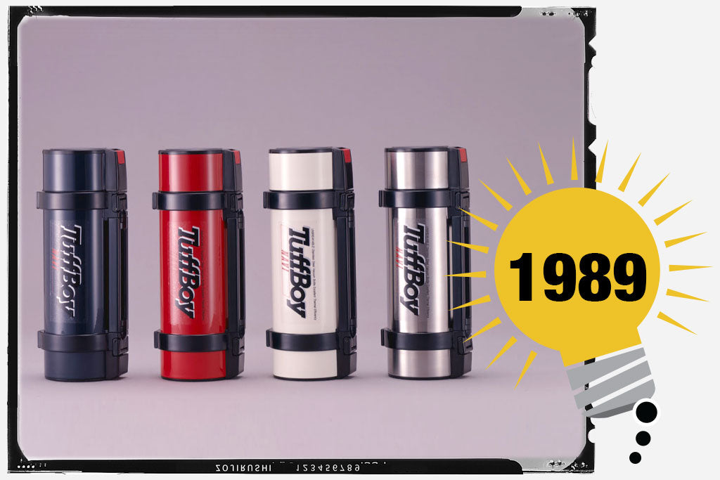 Four Zojirushi Tuff Boy, in navy, red, white, and stainless steel colors. Each unit has a large “TuffBoy” label, with a black handle. Photo is labeled with the year 1989.