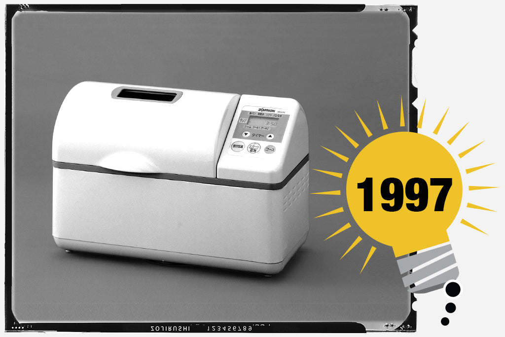 Black and white photo of the first Zojirushi breadmaker that bakes a horizontal 2-lb. loaf. The unit is white. Photo is labeled with the year 1997.