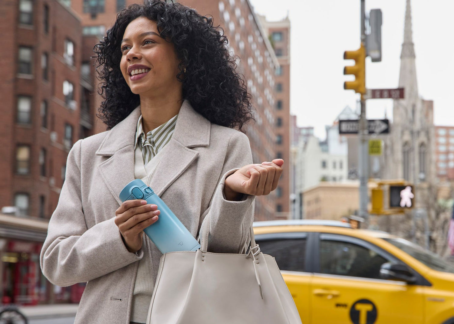 Woman in a city, taking out a Zojirushi GoCafe mug in turquoise white gradient color, from her purse. 
