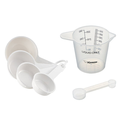 Set of white nested measuring cups, clear liquid measuring cup and spoon on a white background