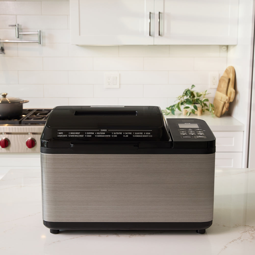Bread machine on a kitchen counter with white cabinets and stove in the background