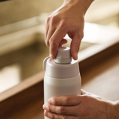 Person opening a white thermos with a blurred background